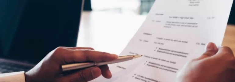 Manos revisando un currículum en una oficina.