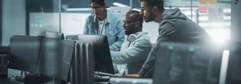 Tres personas trabajando en computadoras en una oficina moderna.