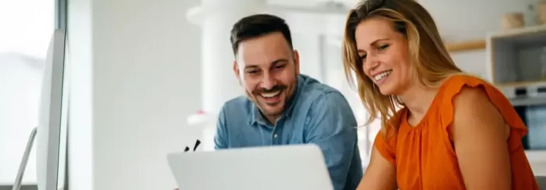 Hombre y mujer mirando la pantalla de ordenador y sonriendo