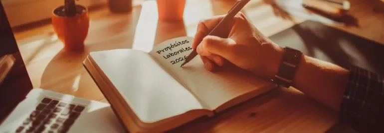 Profesional escribiendo sus objetivos laborales en un cuaderno o revisando metas en ordenador.