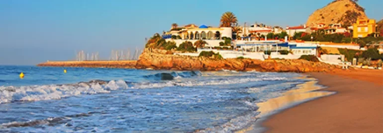 Vista de playa con olas suaves y casas en el fondo al atardecer.