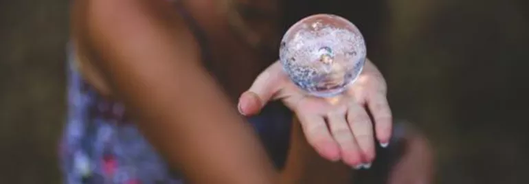 Mano sosteniendo una esfera de cristal transparente.