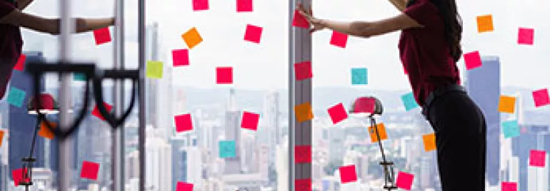 Oficina con notas adhesivas de colores en ventanas. Persona organizando notas.