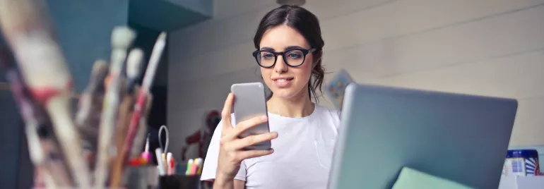 Persona sonriendo mientras usa un teléfono y una computadora portátil.