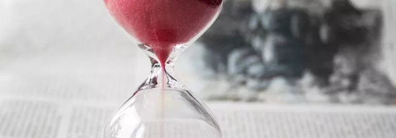 Reloj de arena con arena roja en un fondo de periódico.