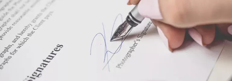 Mano firmando un documento con una pluma plateada.