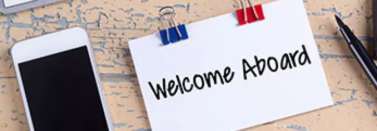 Teléfono, teclado y tarjeta que dice 'Welcome Aboard' sobre una mesa.