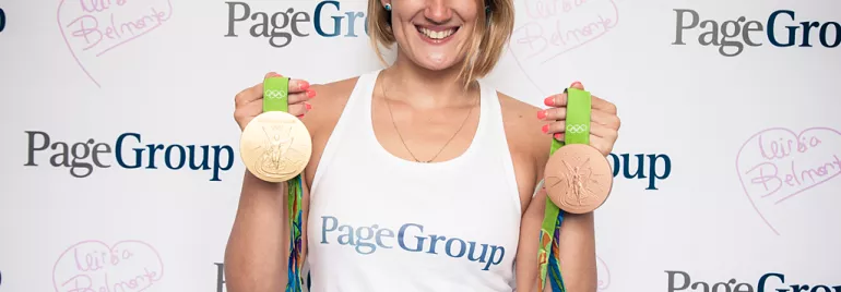 Persona con dos medallas olímpicas sonriendo frente a un banner.