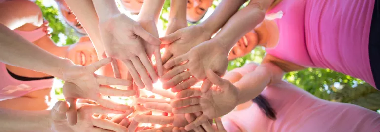 Grupo de personas uniendo manos en círculo al aire libre.