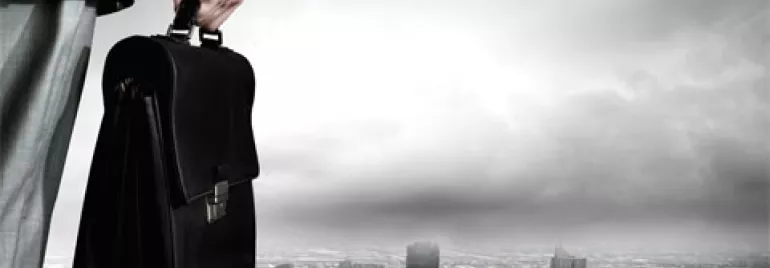 Persona sosteniendo un maletín sobre un paisaje urbano nublado.