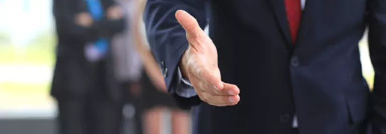 Persona en traje extendiendo la mano para un apretón.