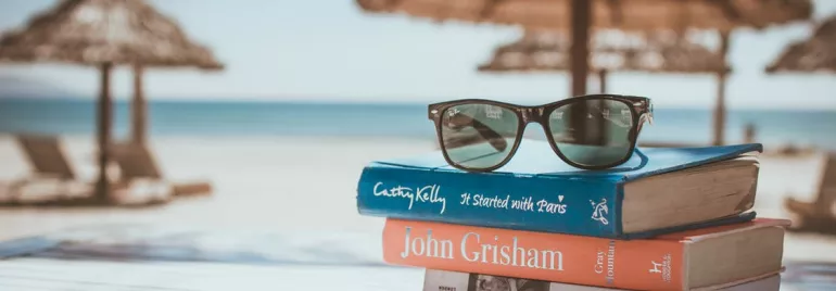 Libros apilados con gafas de sol en la playa.