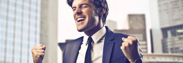 Persona sonriendo triunfalmente con traje en un entorno urbano.