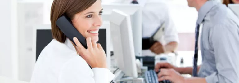 Persona sonriendo mientras habla por teléfono en una oficina.