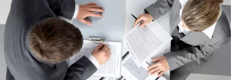 Vista aérea de dos personas en trajes revisando documentos en un escritorio.
