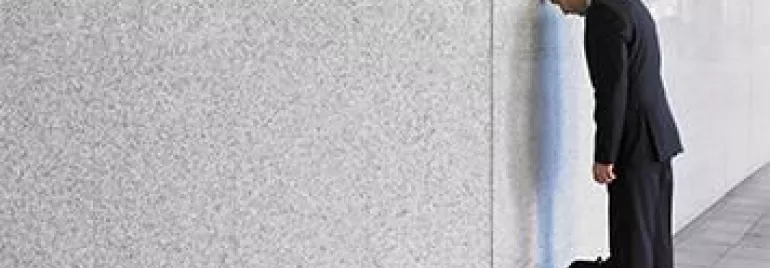 Persona apoyada de cara en una pared con una bolsa de trabajo al lado.