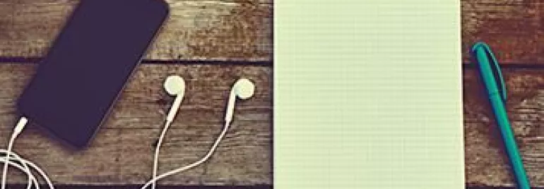 Teléfono, auriculares, libreta y bolígrafo sobre mesa de madera.