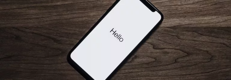 Teléfono móvil en una mesa de madera con la pantalla encendida mostrando 'Hello'.