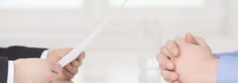 Dos personas sentadas en una mesa, una sostiene un documento.