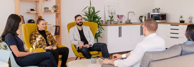 Grupo de personas conversando en una sala moderna con muebles y plantas.