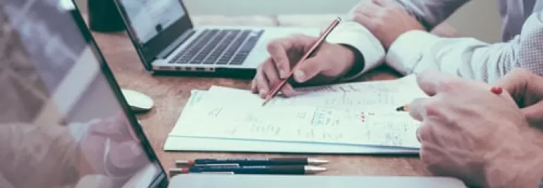 Personas trabajando en documentos y portátiles en una mesa.