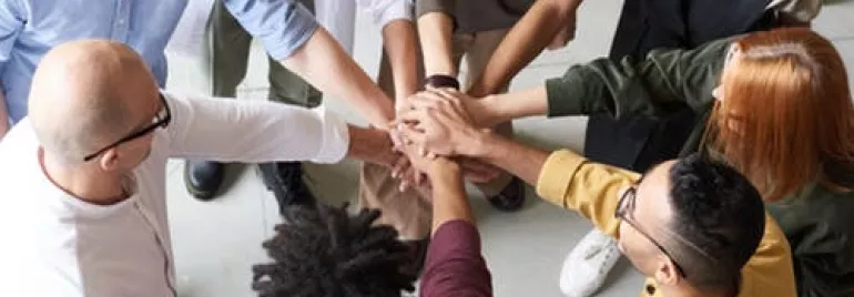 Grupo de personas uniendo manos en un círculo.