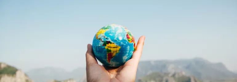 Mano sosteniendo un globo terráqueo pequeño con montañas de fondo.
