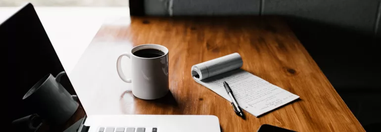 Mesa con portátil, taza de café y cuaderno con bolígrafo.