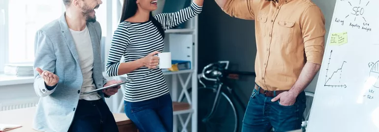 Grupo de personas celebrando en una oficina con una pizarra y una laptop.