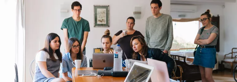 Personas alrededor de una mesa trabajando en computadoras portátiles.