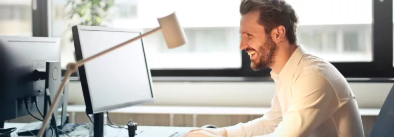 Persona sonriendo mientras trabaja en la computadora en una oficina luminosa.
