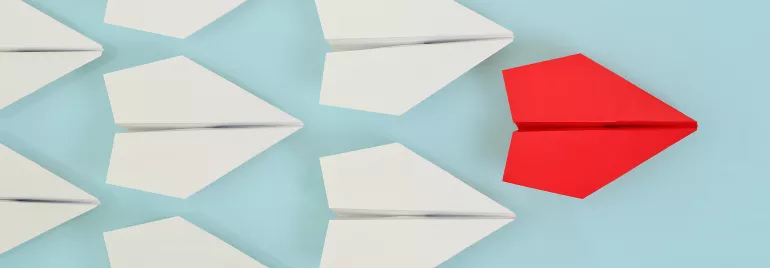 Aviones de papel blancos y uno rojo sobre fondo azul.