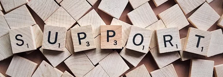 Letras de Scrabble formando la palabra 'SUPPORT' sobre bloques de madera.
