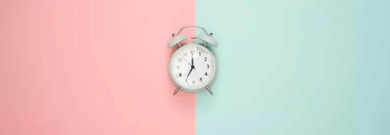 Reloj despertador sobre fondo dividido en rosa y azul.