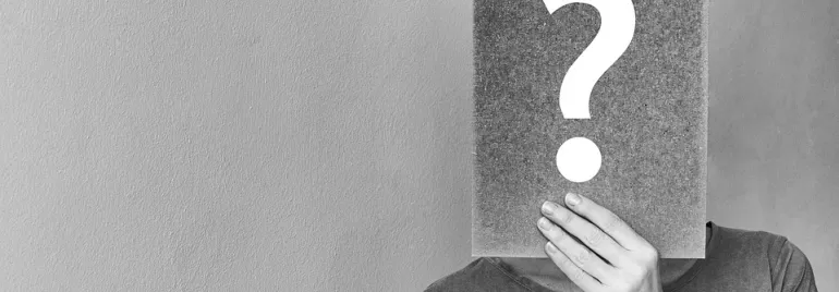 Persona cubre su cara con un cartel de signo de interrogación.