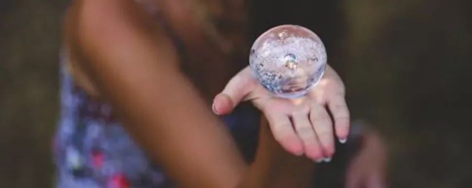 Mano sosteniendo una esfera de cristal transparente.