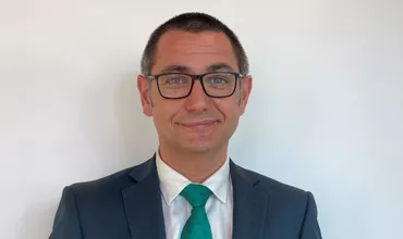 Persona con traje azul y corbata verde, fondo blanco.