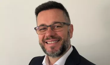 Persona sonriendo, con gafas y barba, fondo blanco.