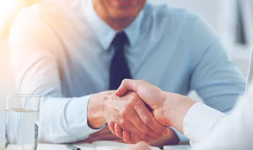 Dos personas estrechando manos en una reunión de negocios.