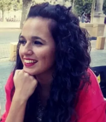 Persona sonriendo al aire libre, con cabello rizado y chaqueta roja.